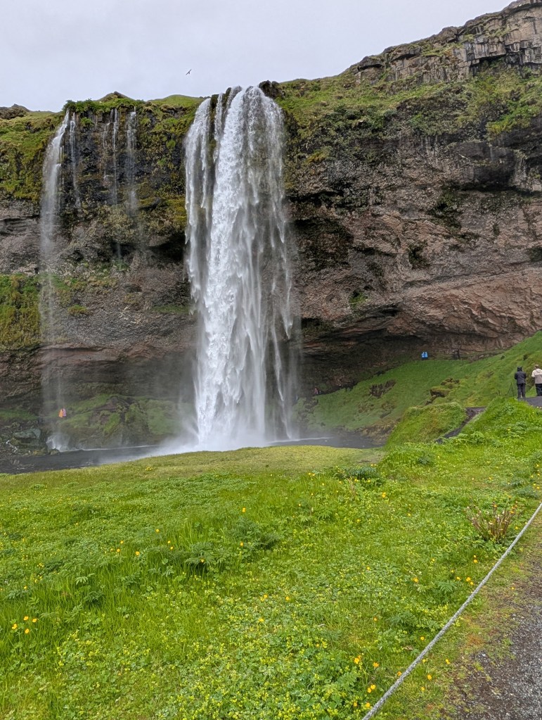 A beautiful waterfall cascading down a rocky cliff surrounded by lush greenery, with visitors standing nearby and enjoying the view.