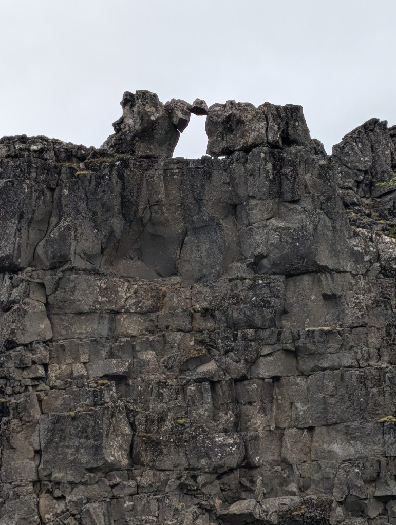 A close-up of a rocky cliff with a heart-shaped arch at the top, surrounded by textured rock formations.