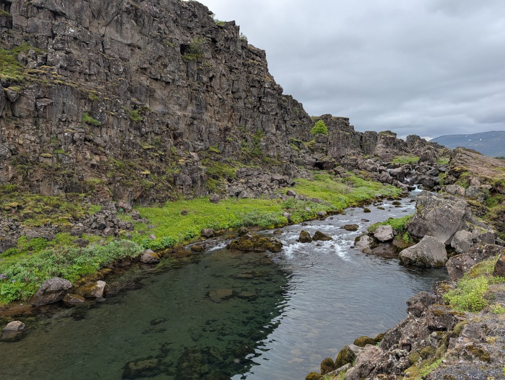 A serene landscape featuring a winding river surrounded by rocky cliffs and lush greenery under an overcast sky.