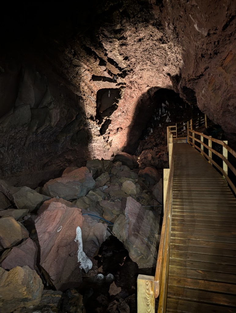 A dimly lit cave featuring a wooden pathway and scattered rocks on the ground.