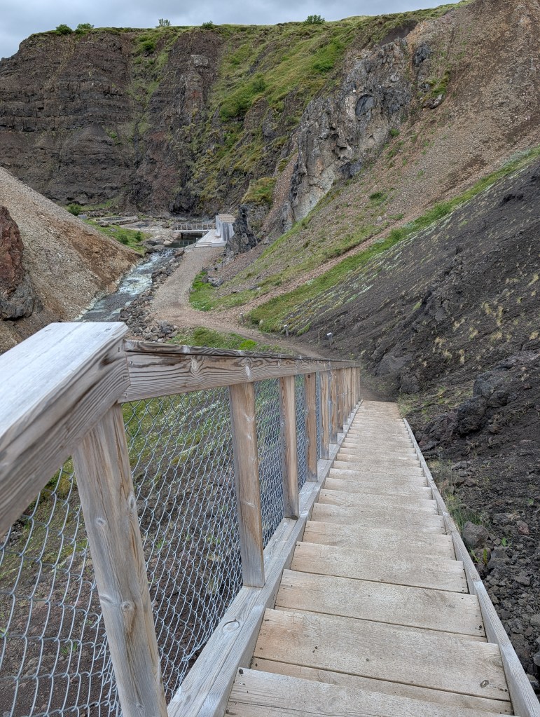 A wooden staircase leading down into a rocky canyon with steep cliffs and a path visible at the bottom.