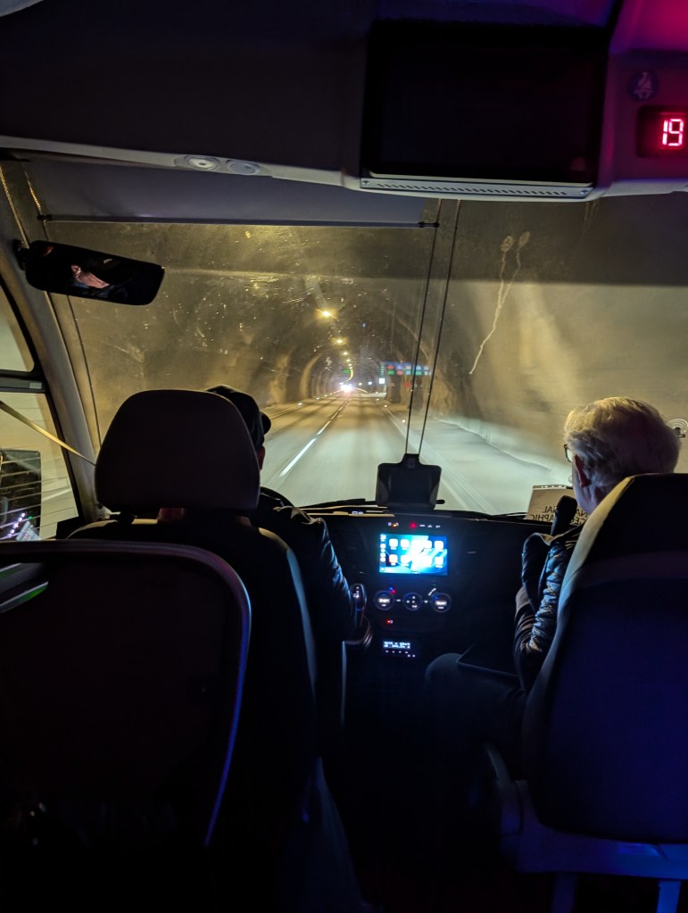 Interior view of a vehicle driving through a tunnel, showing the dashboard and two passengers in the front seats.
