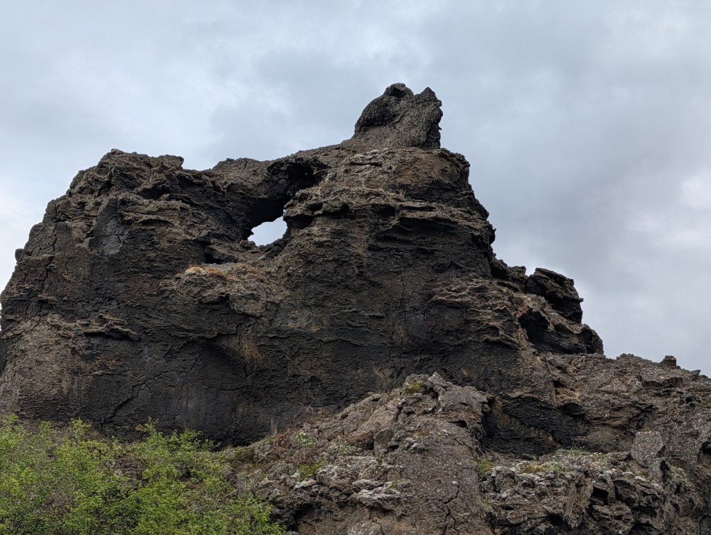 A jagged lava rock formation featuring a circular hole near the top, under a cloudy sky.