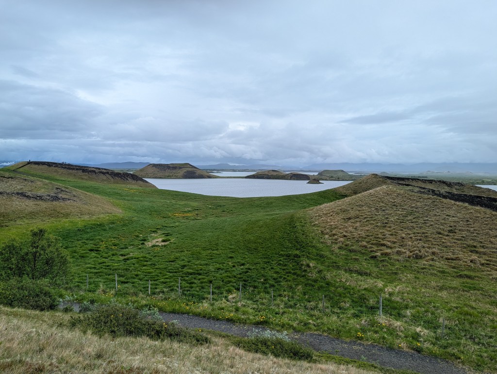 A scenic view of rolling green hills surrounding a calm lake under a cloudy sky.