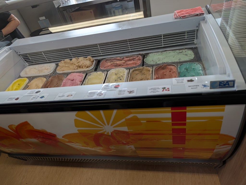 A display of various ice cream flavors in a glass-fronted freezer, with colorful containers and a decorative design on the front.