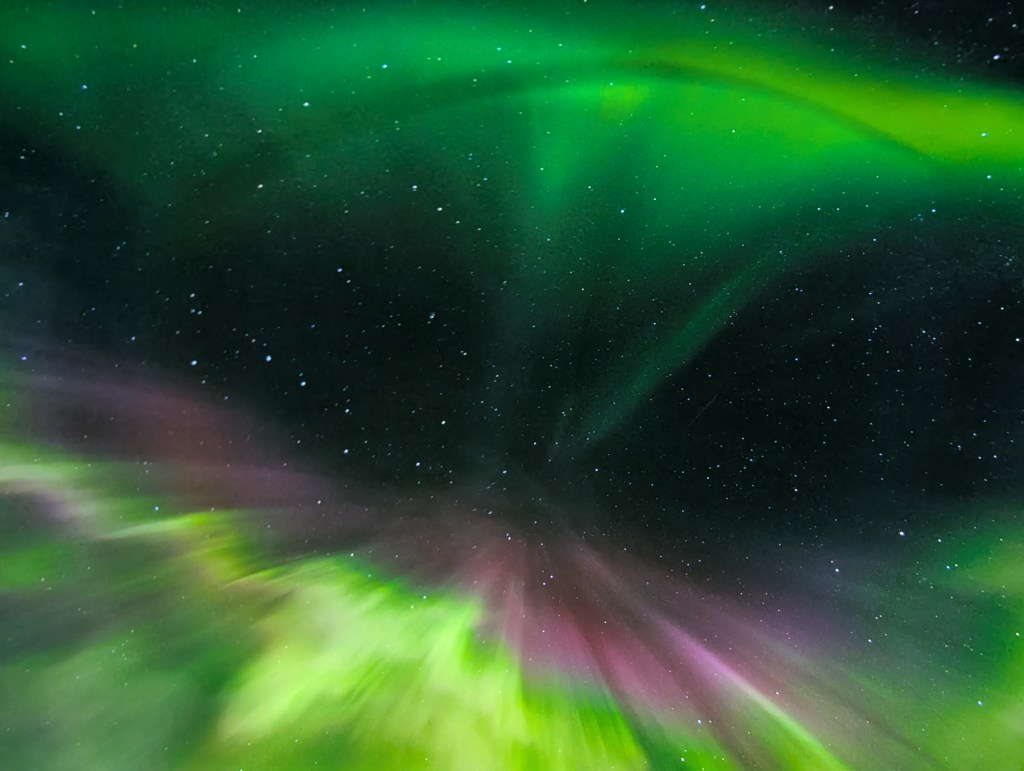 A vibrant display of the aurora borealis with swirling green and purple lights against a starry night sky.