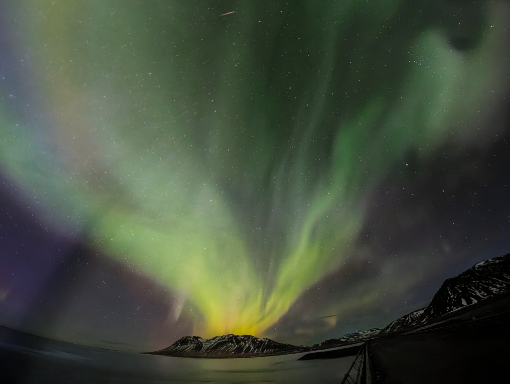 A vibrant aurora borealis lighting up the night sky over a snowy mountain landscape, with swirling green and purple lights and a star-filled background.
