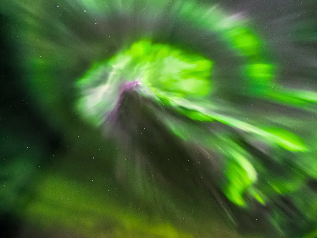 A vibrant display of green and purple auroras swirling across a night sky, creating a sense of motion and depth.