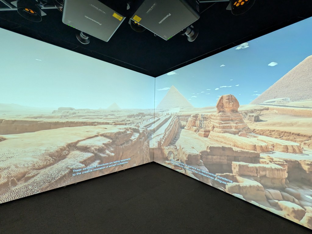 A virtual reality environment showcasing a panoramic view of the pyramids and the Sphinx in a desert landscape, with informative text displayed on the walls.