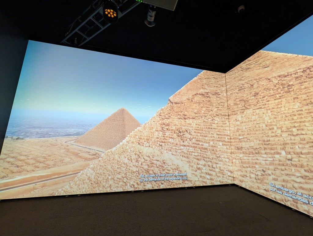 A panoramic view of the pyramids at Giza, displaying the Great Pyramid and its surroundings on a large digital screen.